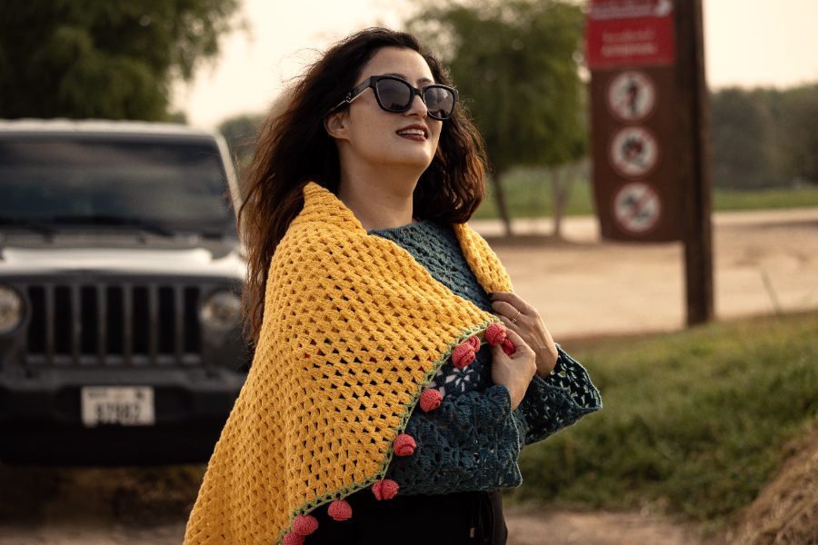 Nish wearing a marigold crochet shawl over a teal top